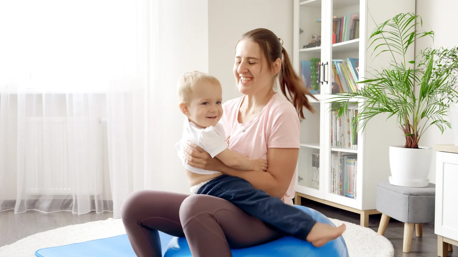mother holding toddler while sitting on exercise
